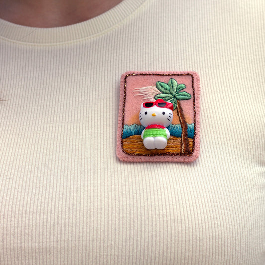 Closeup of a Handmade embroidered Hello Kitty brooch worn on a white t-shirt.