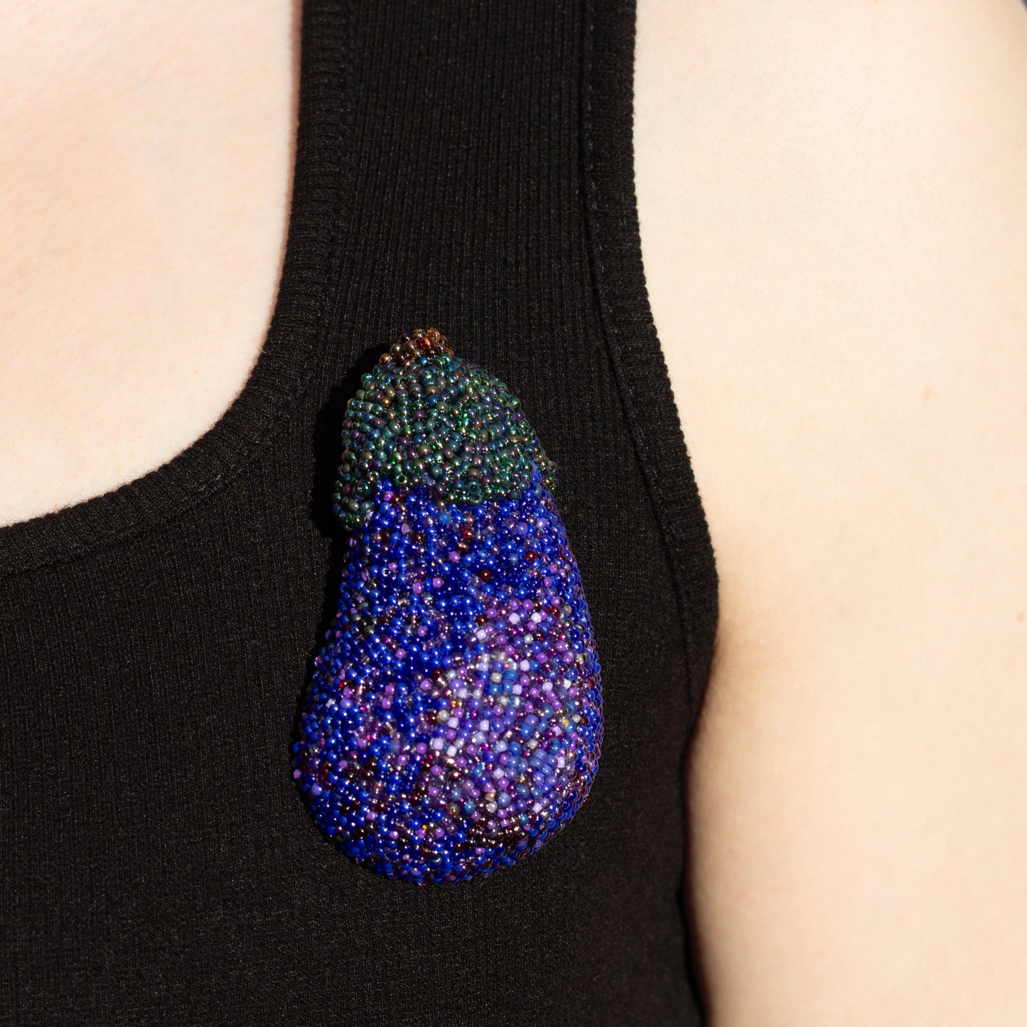 Closeup of a handmade purple beaded eggplant brooch worn on a black tank top.
