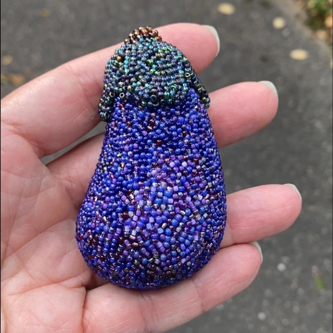 Hand holding a beaded purple eggplant brooch in the sunlight.