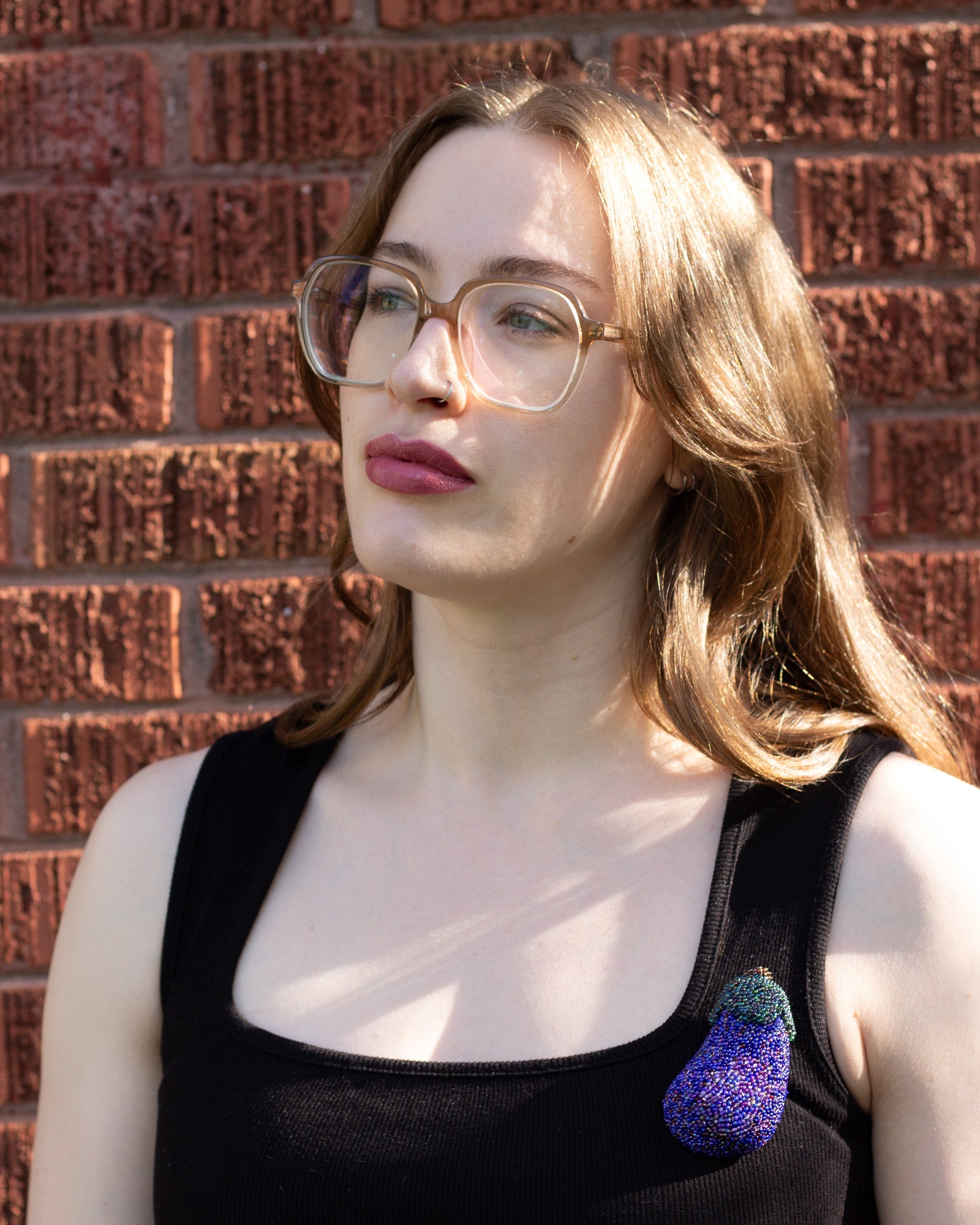 Purple handmade beaded eggplant brooch worn on a black tank top by a young woman.