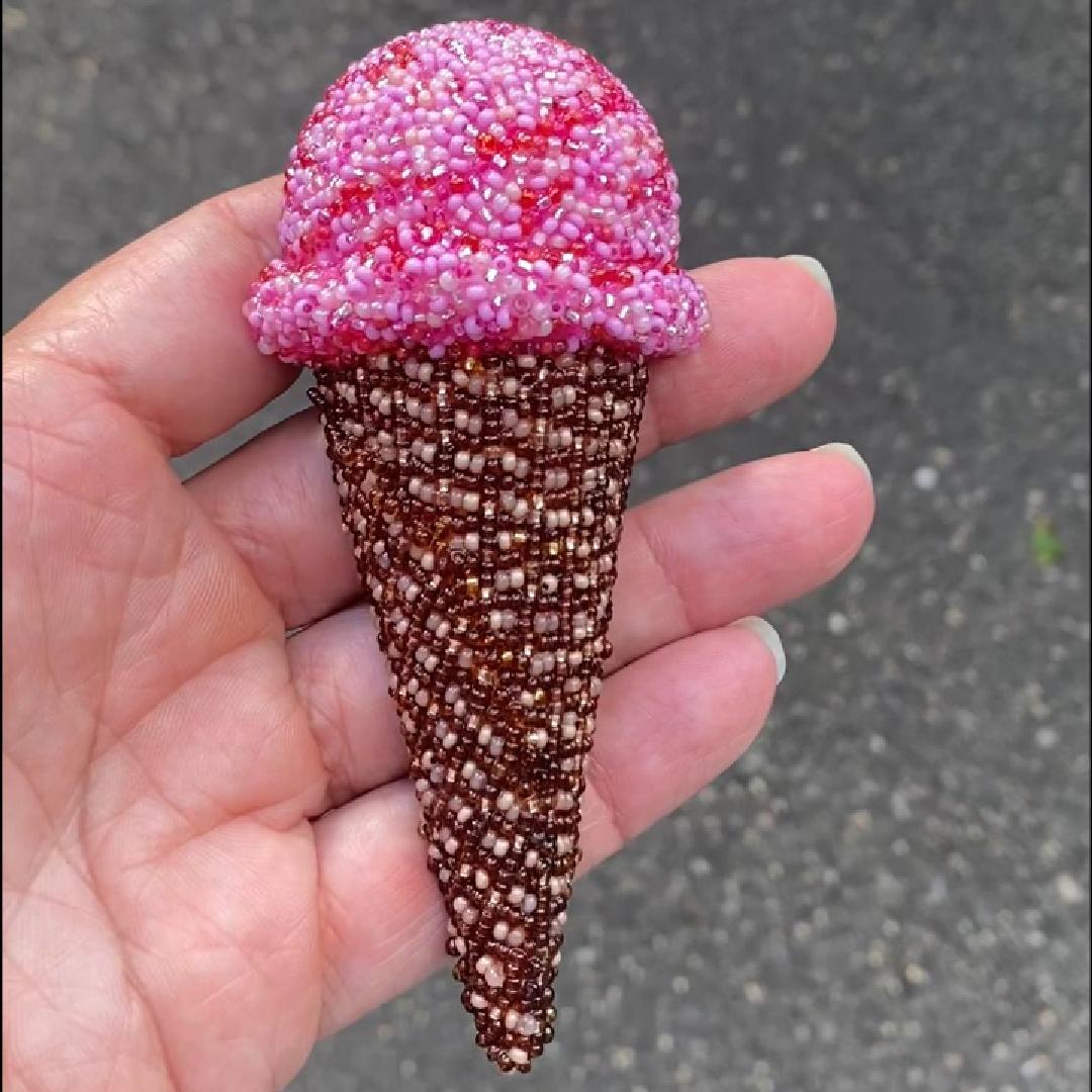 Hand holding a pink beaded ice cream cone brooch in the sunlight.