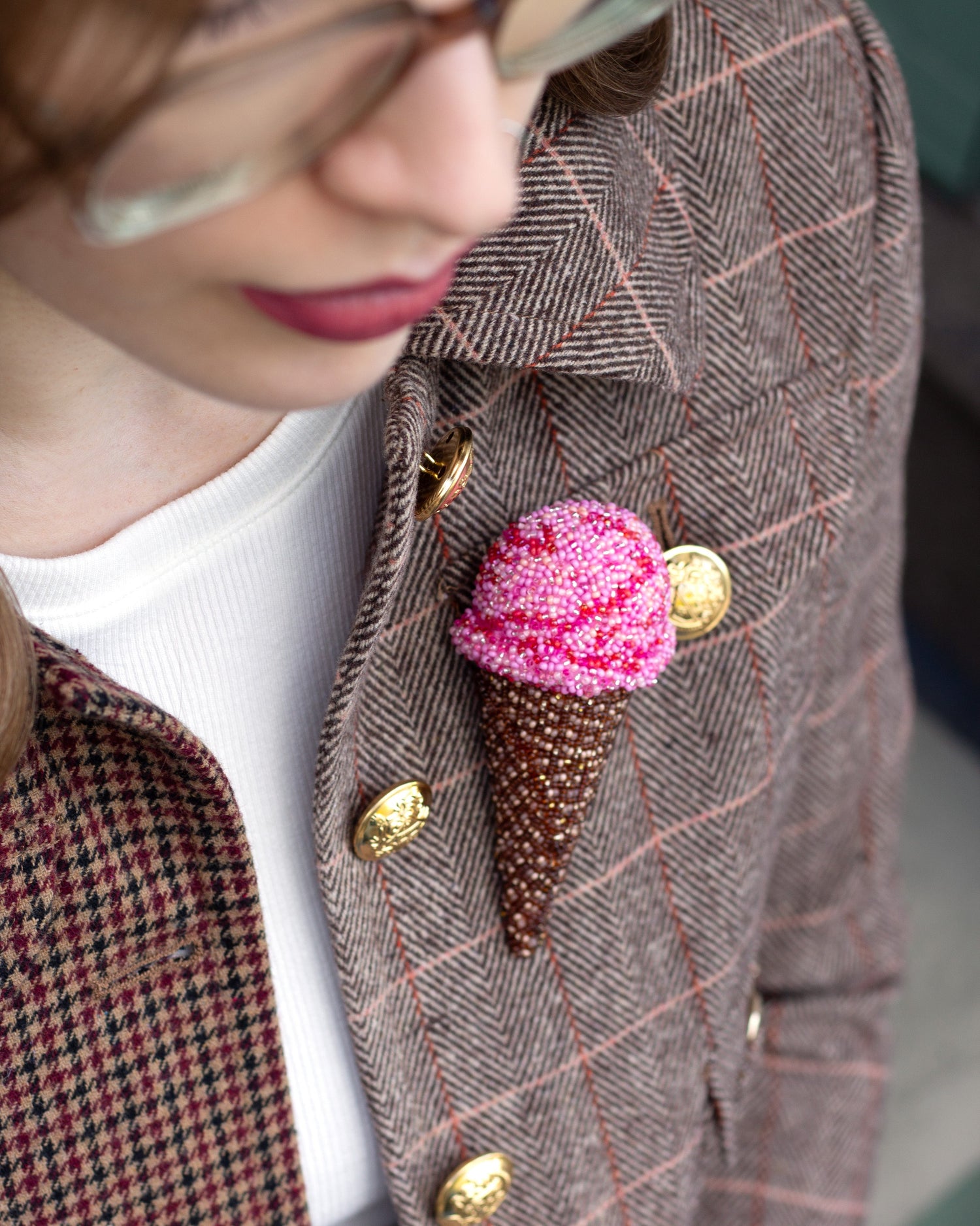 Handmade beaded ice cream cone brooch worn on a patterned jacket by a young woman.