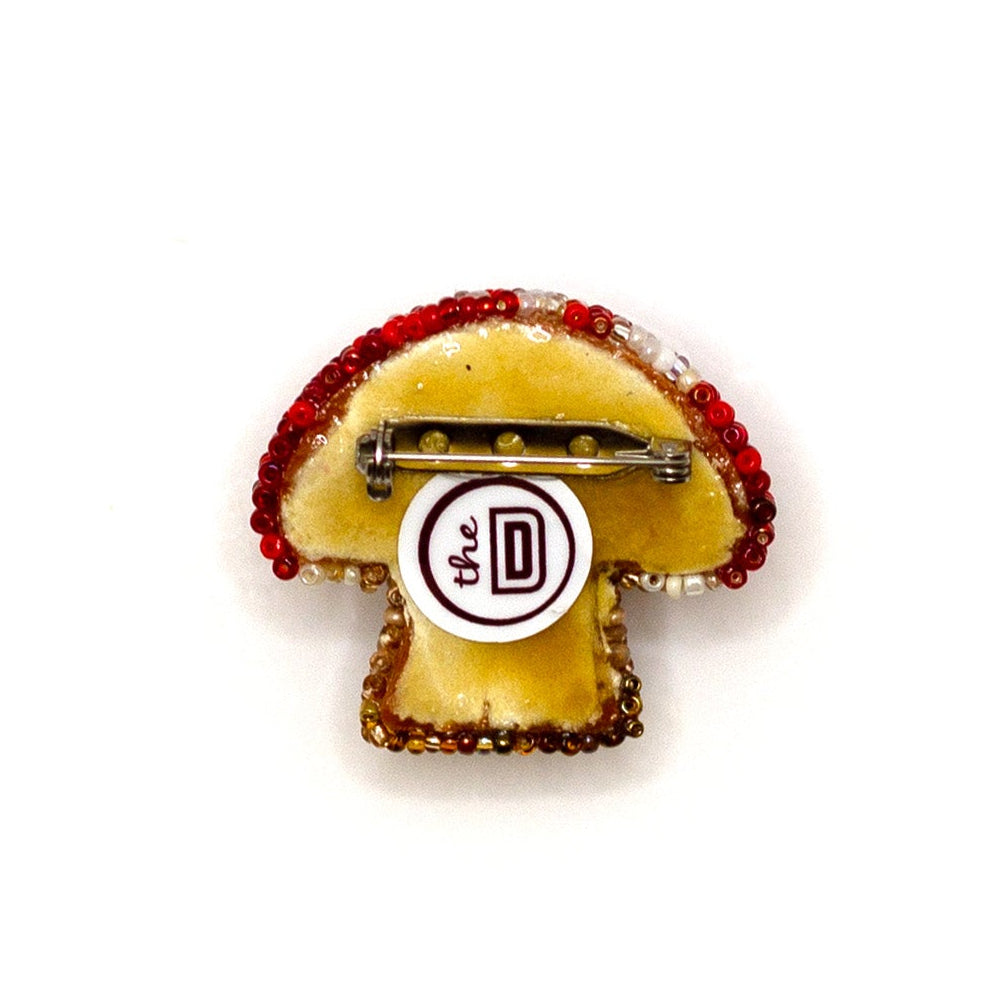 Back view of a handmade beaded mushroom brooch on a white background showing pin fastener.