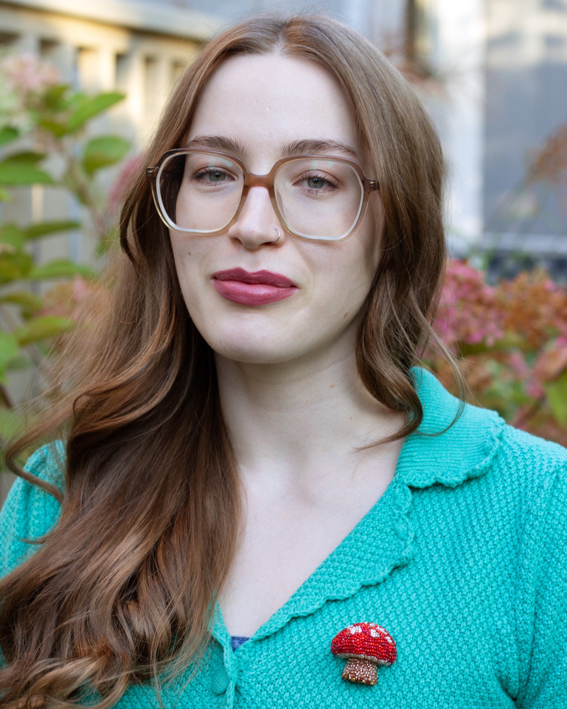 Red and white handmade beaded mushroom brooch worn on a green cardigan by a young woman.