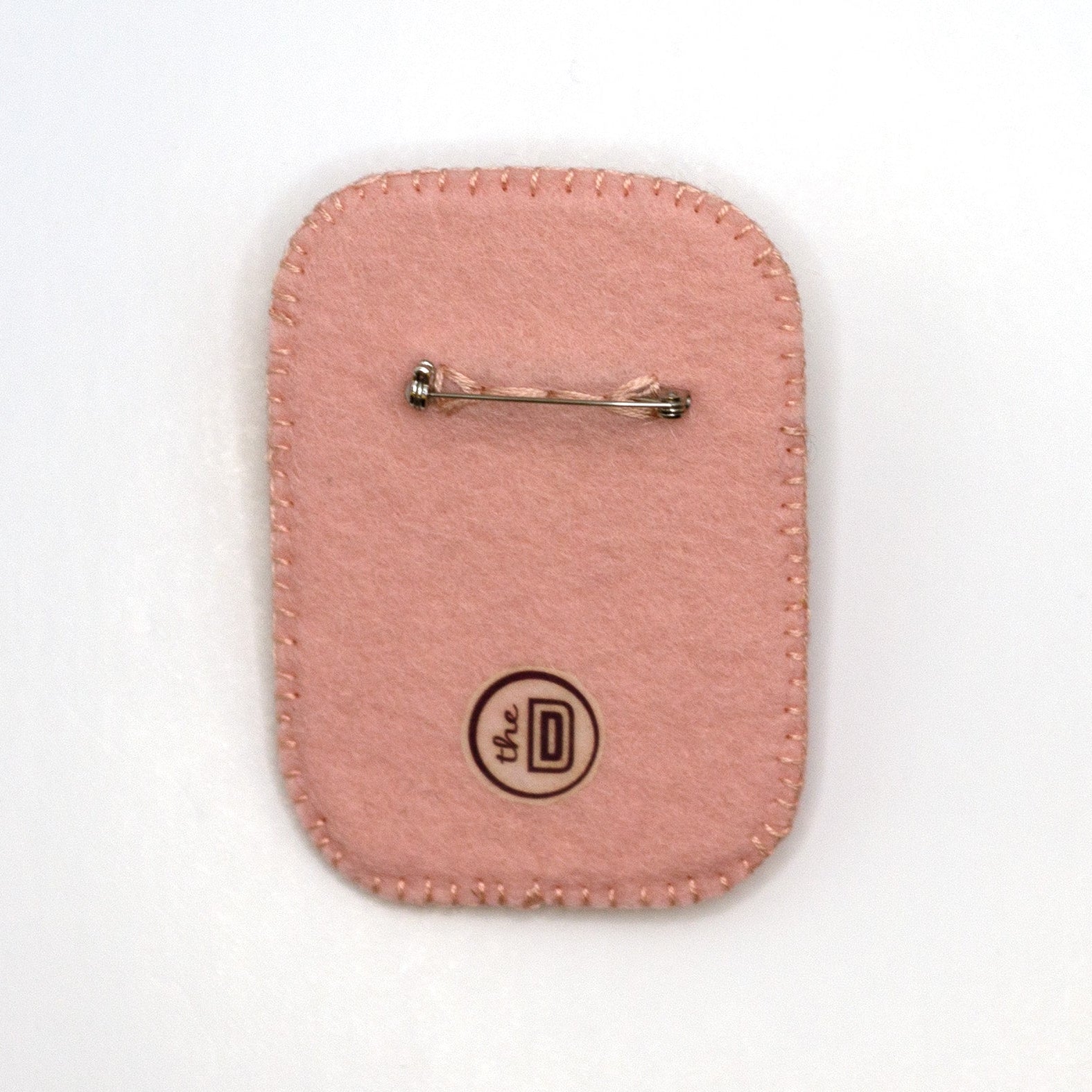 Back view of a Happi Twozie brooch embroidered with a daisy on a white background showing pin fastener.