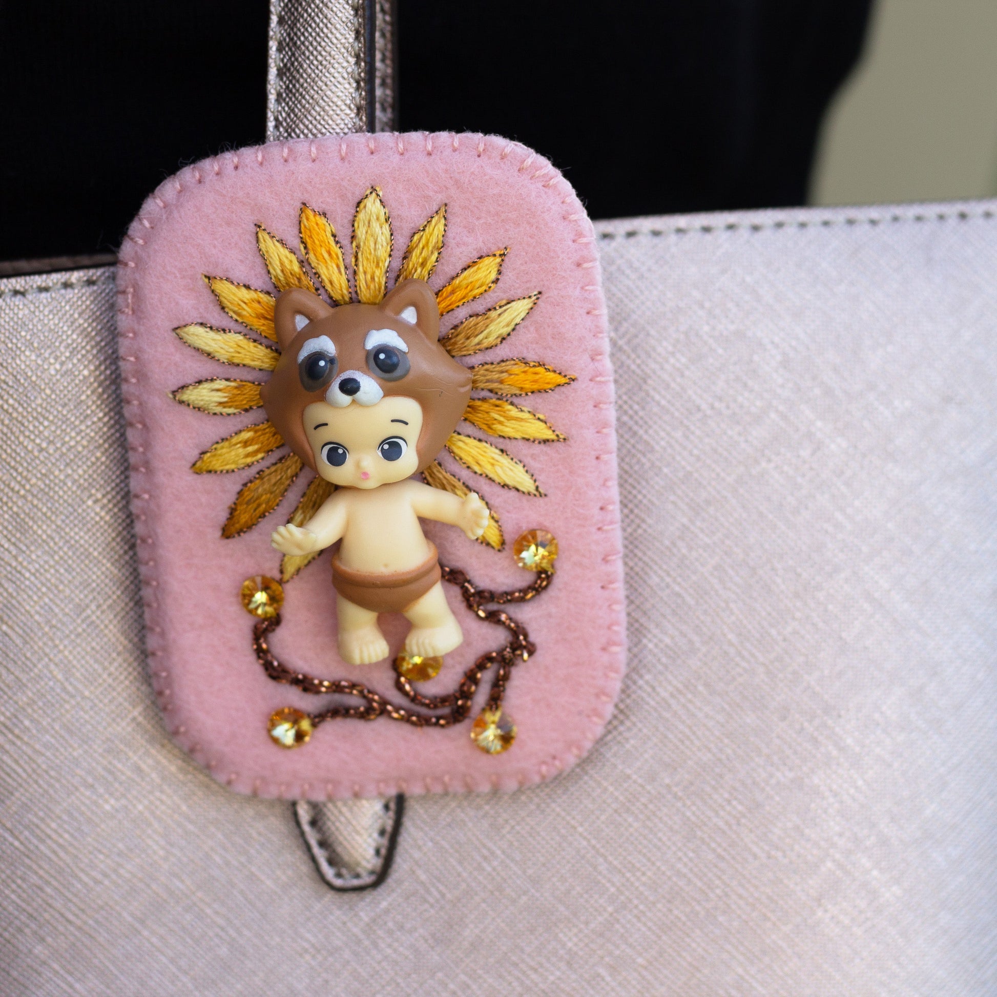 Closeup of a handmade daisy embroidered Happi Twozie brooch worn on a pink purse.