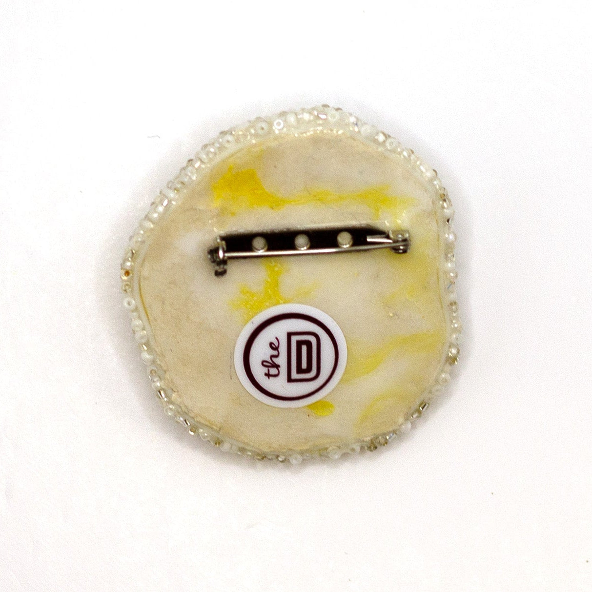 Back view of a handmade beaded fried egg brooch on a white background showing pin fastener.