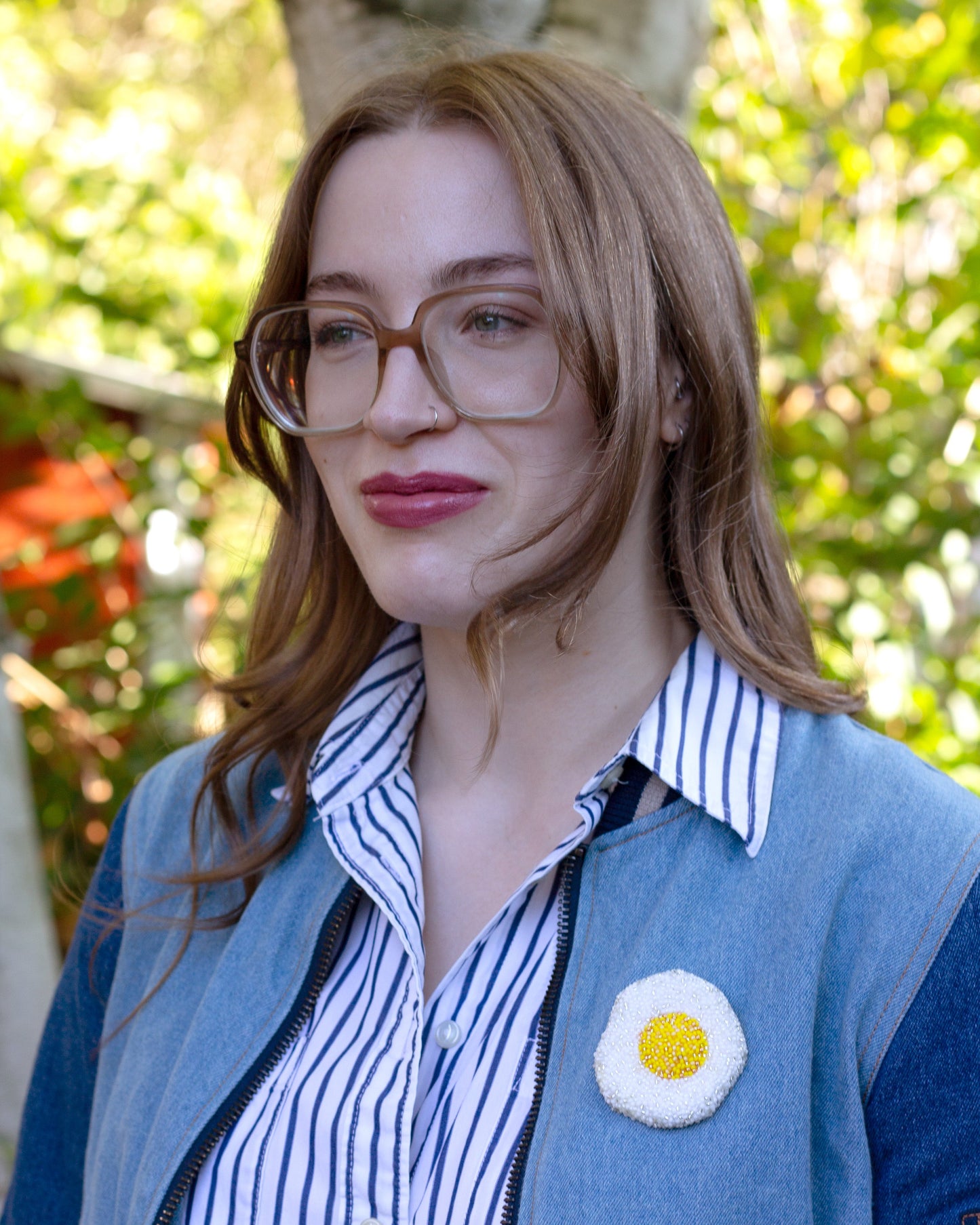 A handmade fried egg beaded brooch worn on a light denim jacket by a young woman.