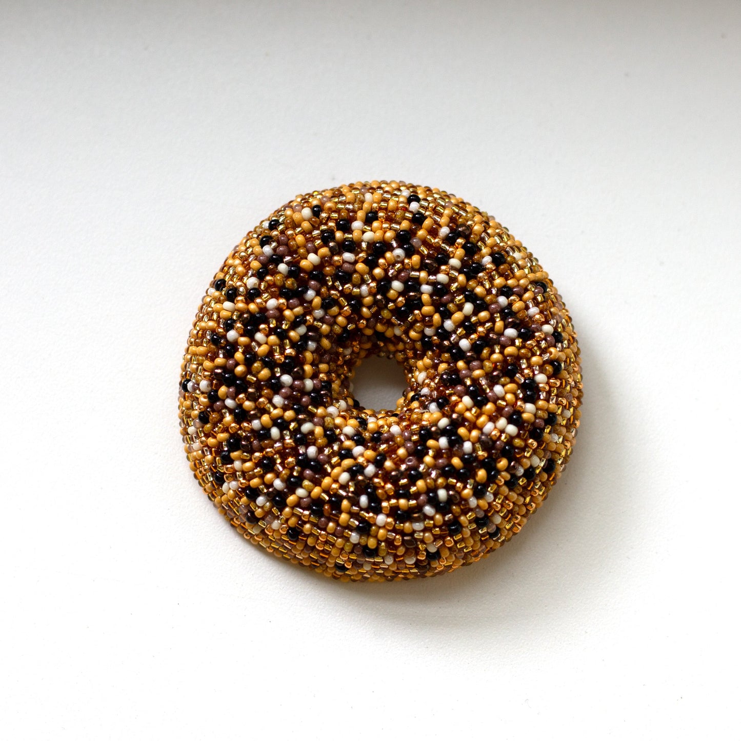 A beaded everything bagel brooch, photographed on a clean white background.