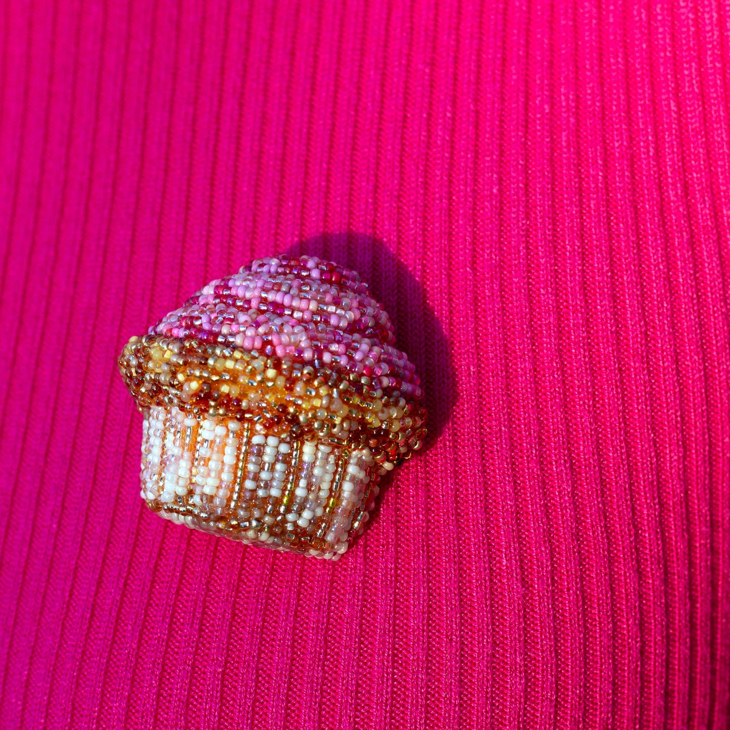 Closeup of a handmade beaded pink frosted cupcake brooch worn on a bright pink sweater.