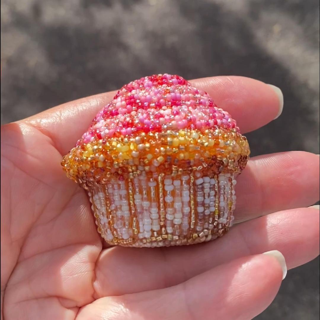 Hand holding a beaded pink frosted cupcake brooch in the sunlight.