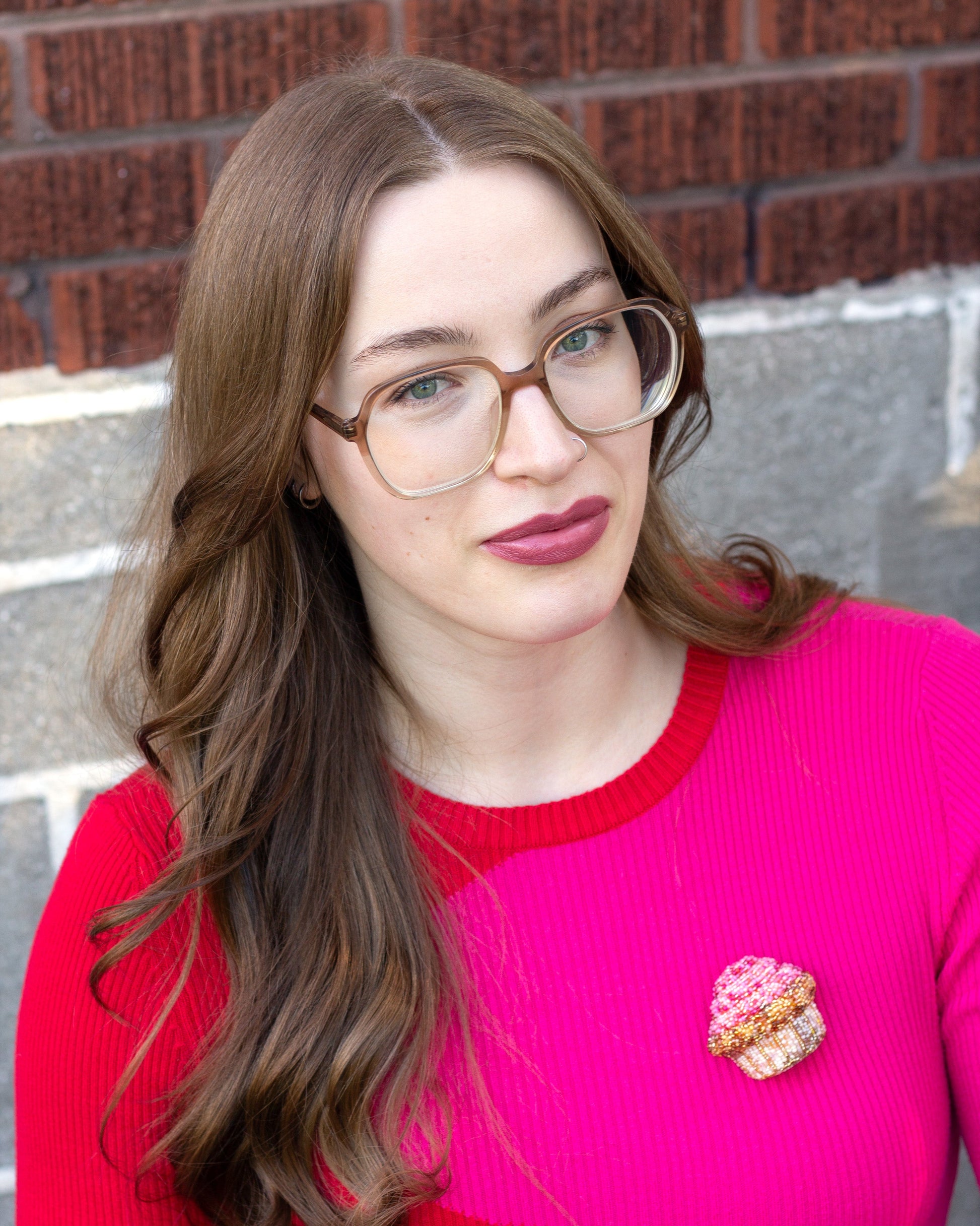 Handmade beaded pink frosted cupcake brooch worn on a bright pink sweater by a young woman.