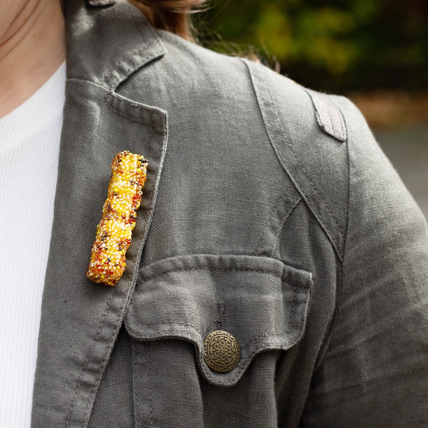 Closeup of a handmade beaded French fry brooch worn on a khaki coloured jacket lapel.
