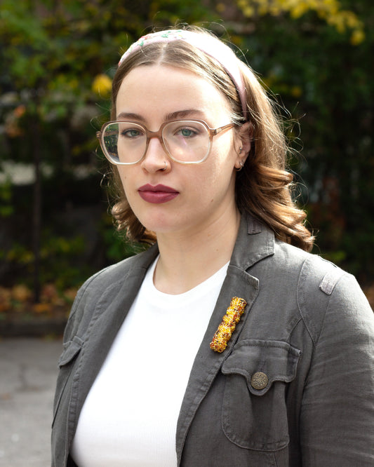 Handmade beaded French fry brooch worn on a khaki coloured jacket lapel by a young woman.