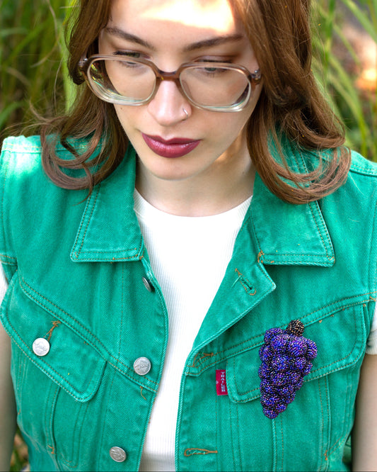 Purple handmade beaded grape bunch brooch worn on a green vest pocket by a young woman.