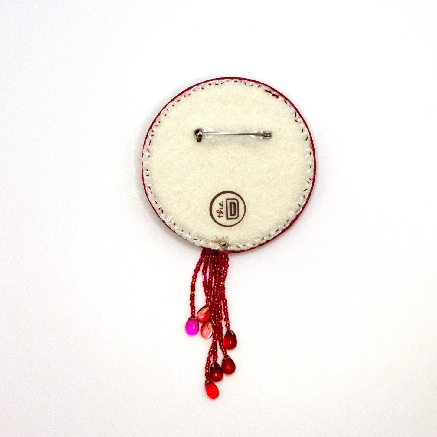Back view of a handmade brooch featuring a sequined heart cradled by doll hands on a white background showing pin fastener.