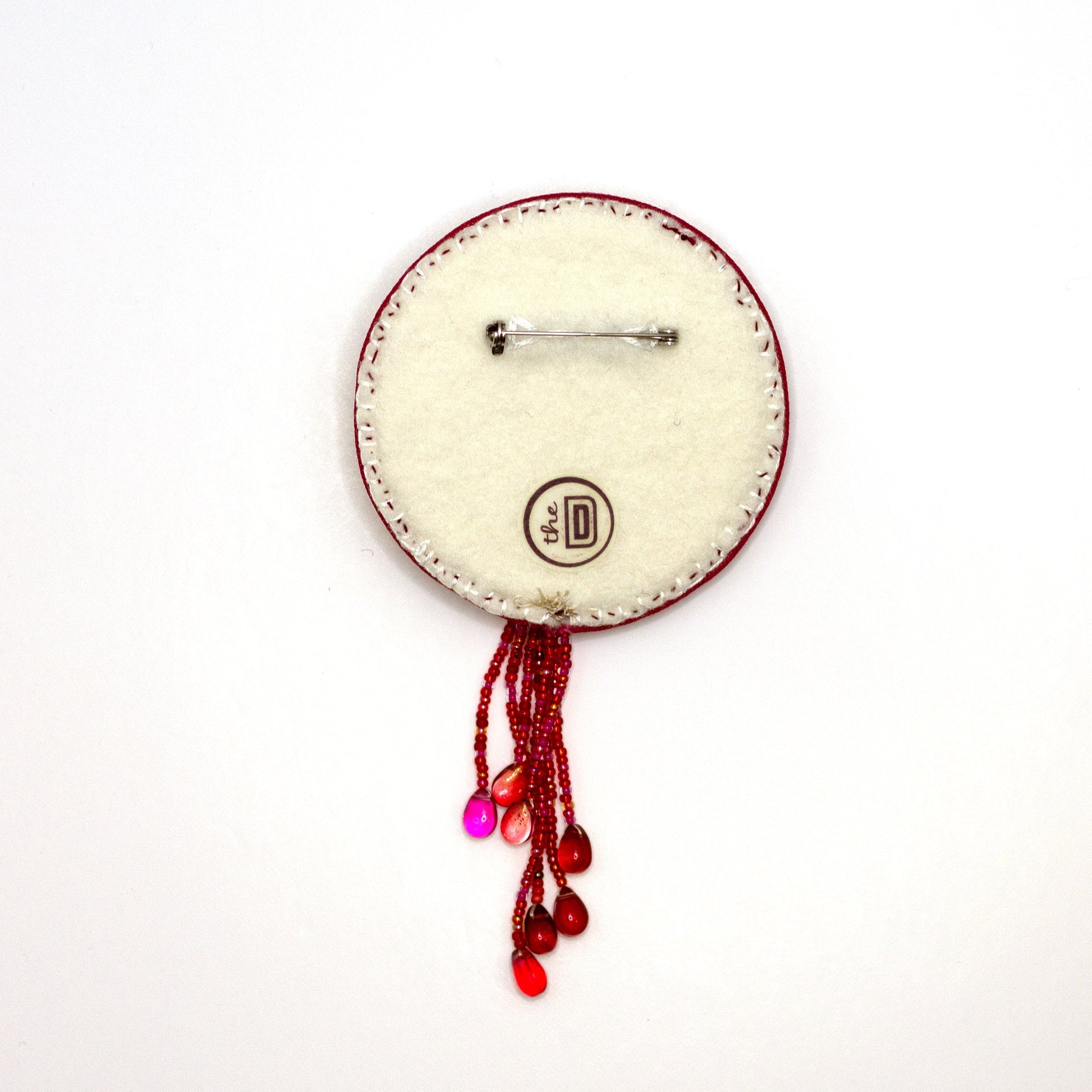 Back view of a handmade brooch featuring a sequined heart cradled by doll hands on a white background showing pin fastener.
