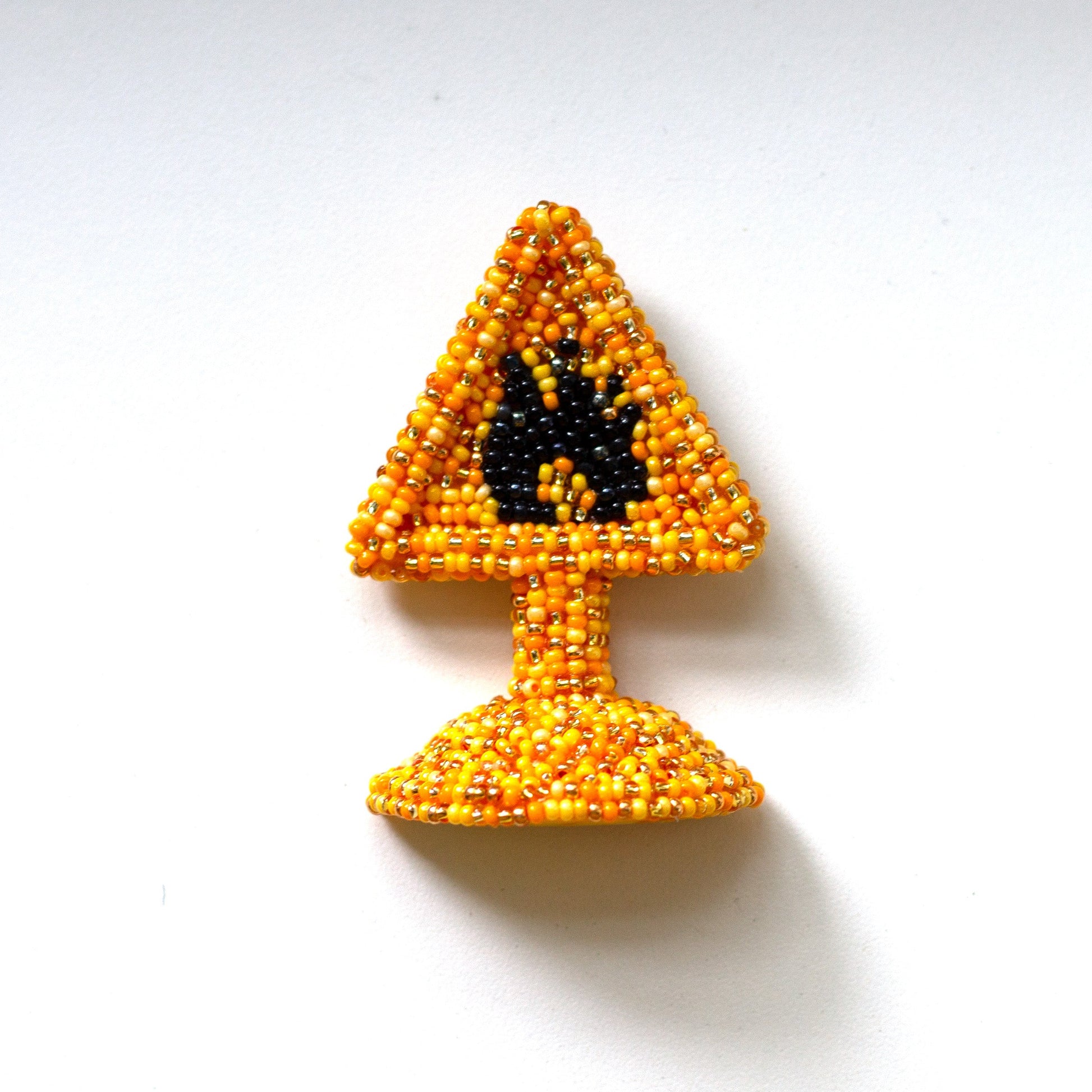 A small beaded warning sign pin featuring a yellow triangle with a black highly flammable symbol above a yellow base, photographed on a plain white background.