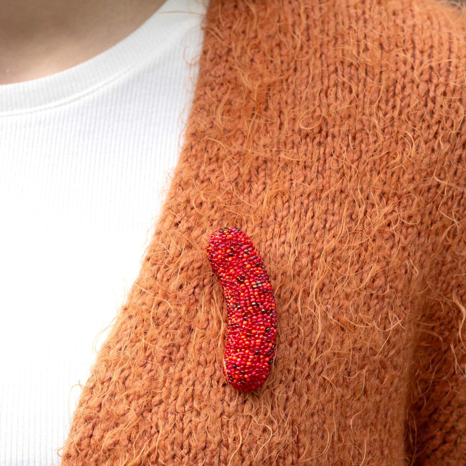 Closeup of a handmade beaded hot dog brooch worn on an orange cardigan.