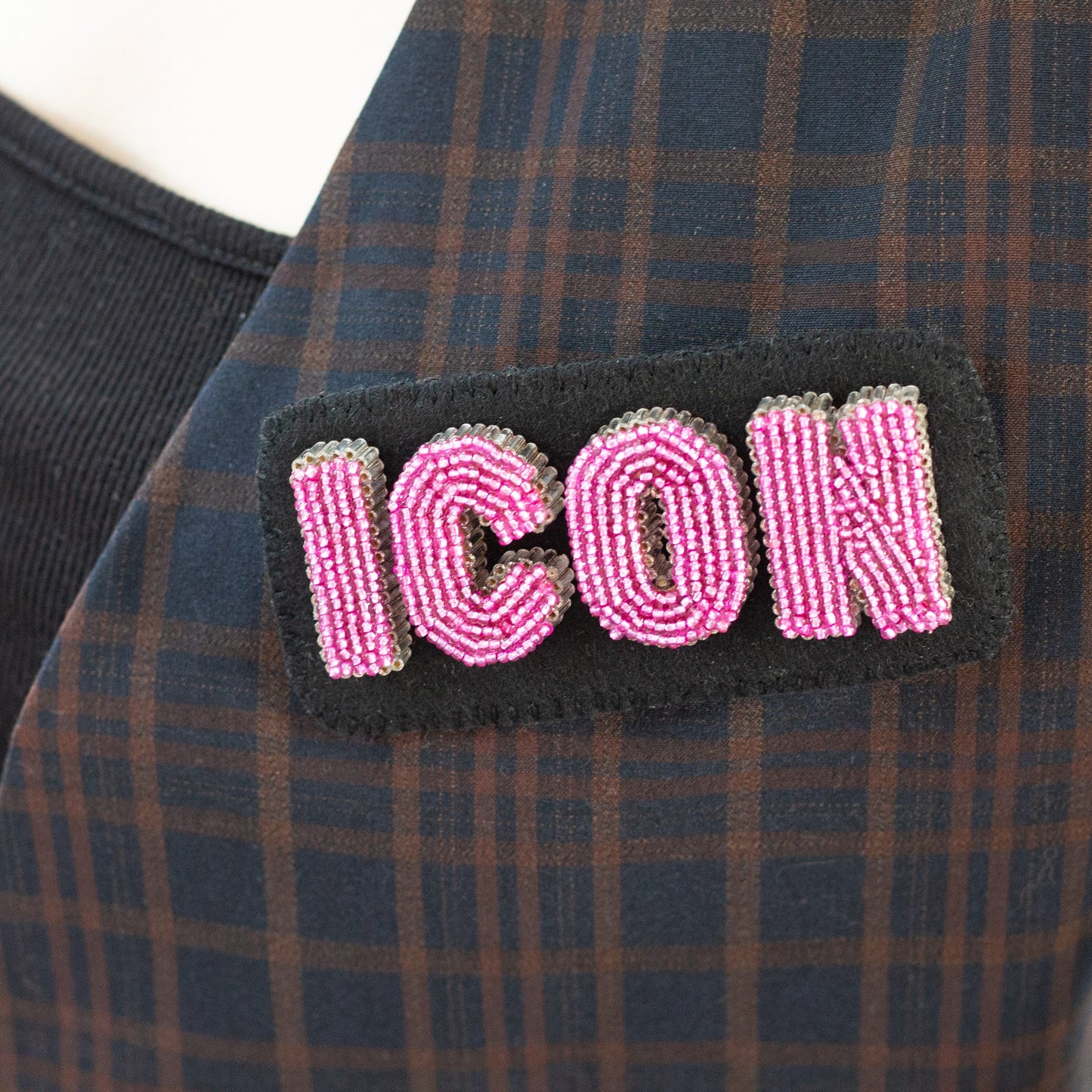 Closeup of a handmade beaded ICON letter brooch worn on a plaid blazer.