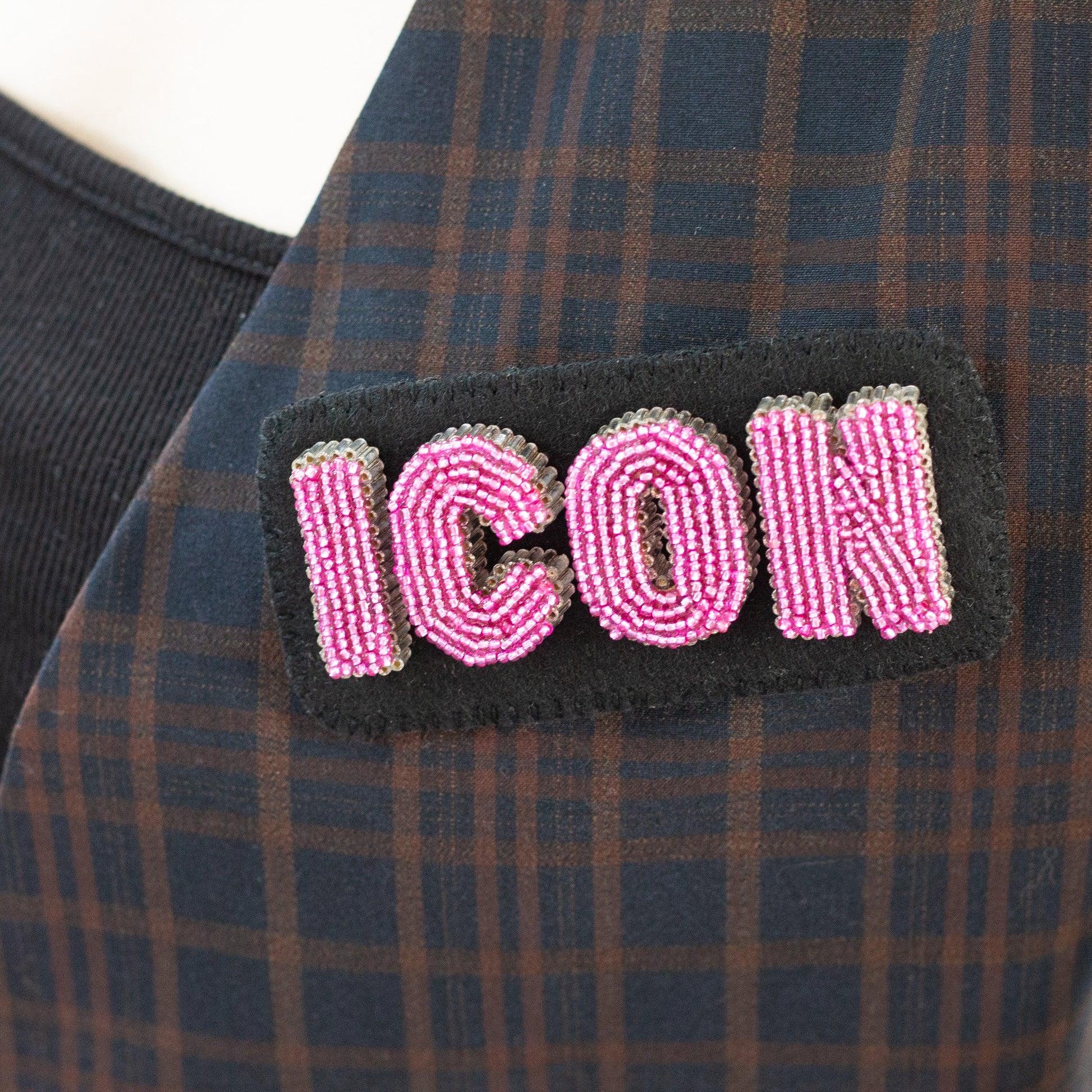 Closeup of a handmade beaded ICON letter brooch worn on a plaid blazer.