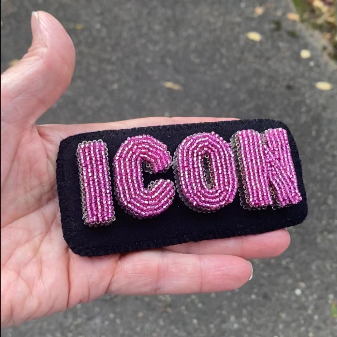 Hand holding a beaded ICON letter brooch in the sunlight.