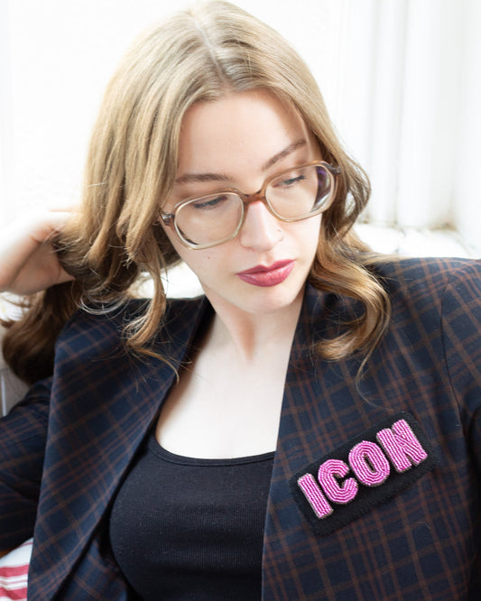 Handmade beaded ICON letter brooch worn on a plaid blazer by a young woman.