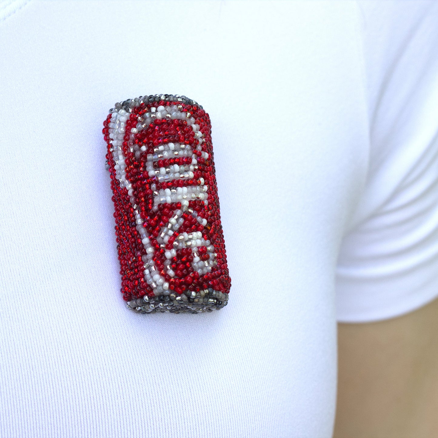 Closeup of a beaded Coke pop can brooch worn on a white t-shirt.