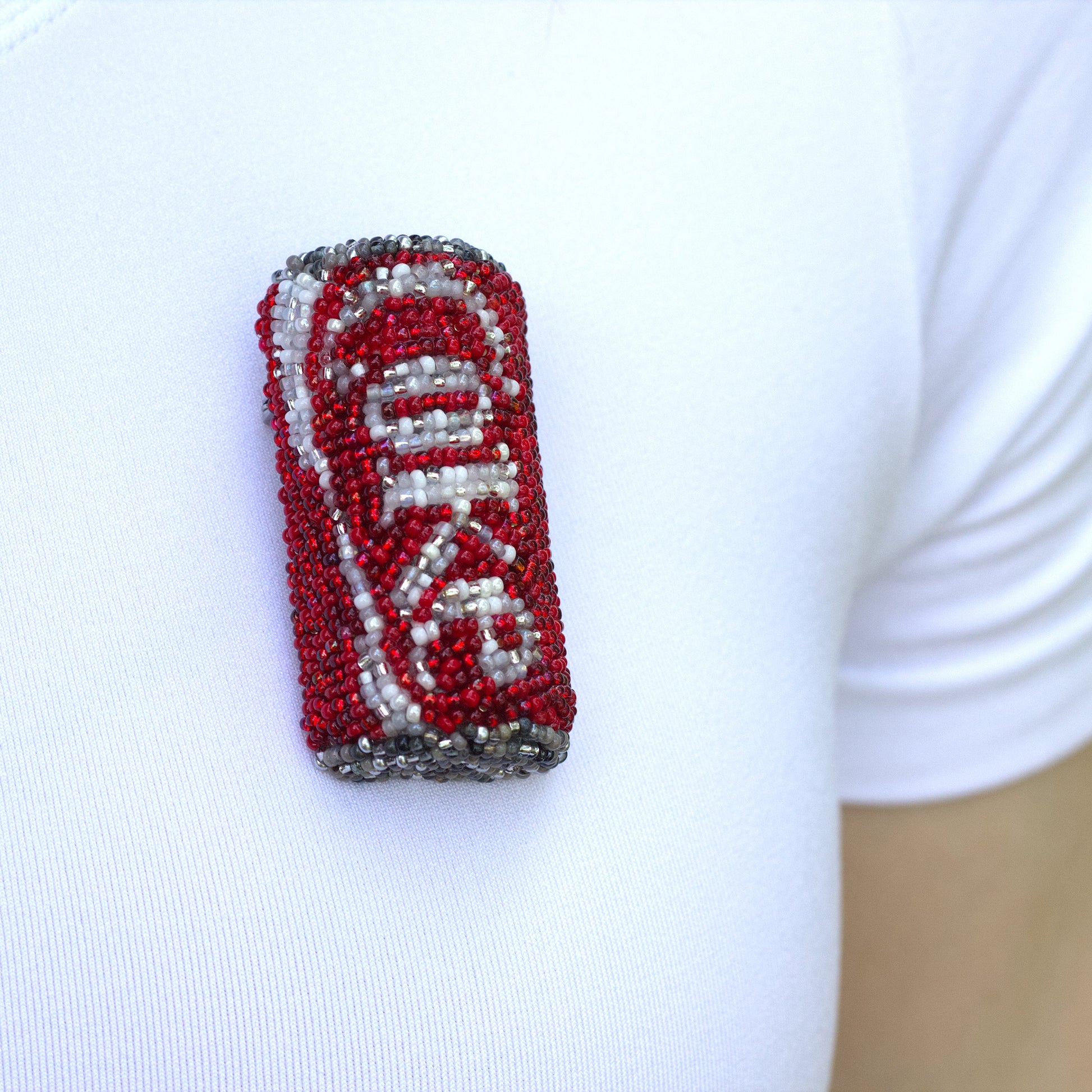 Closeup of a beaded Coke pop can brooch worn on a white t-shirt.