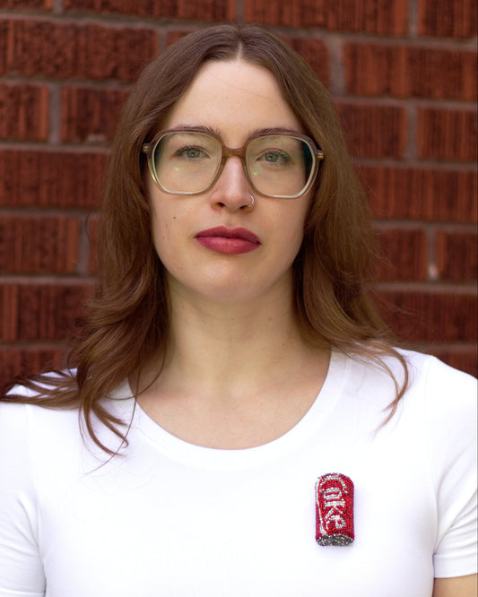 Handmade beaded Coke pop can brooch worn on a white t-shirt by a young woman.