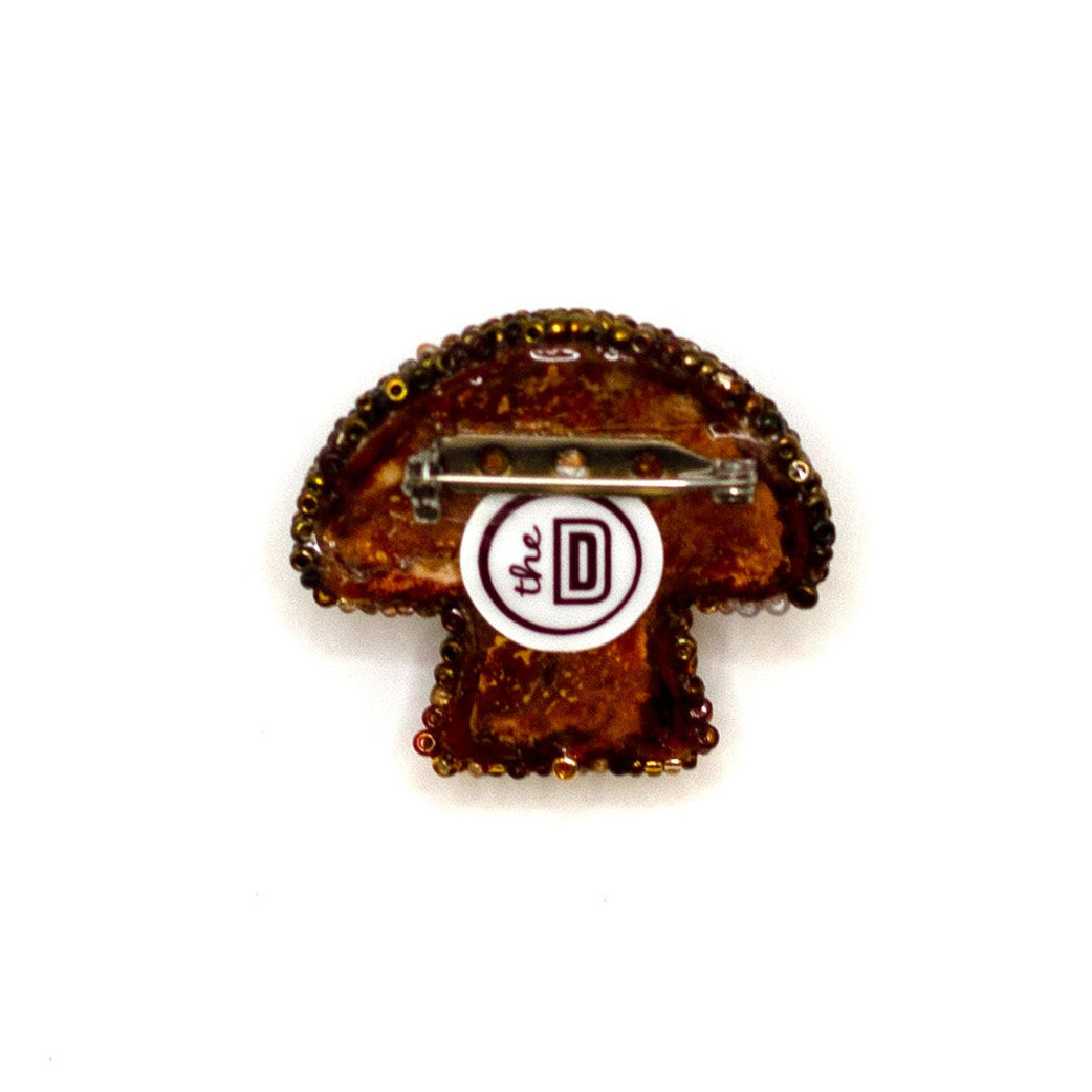 Back view of a handmade beaded brown mushroom brooch on a white background showing pin fastener.