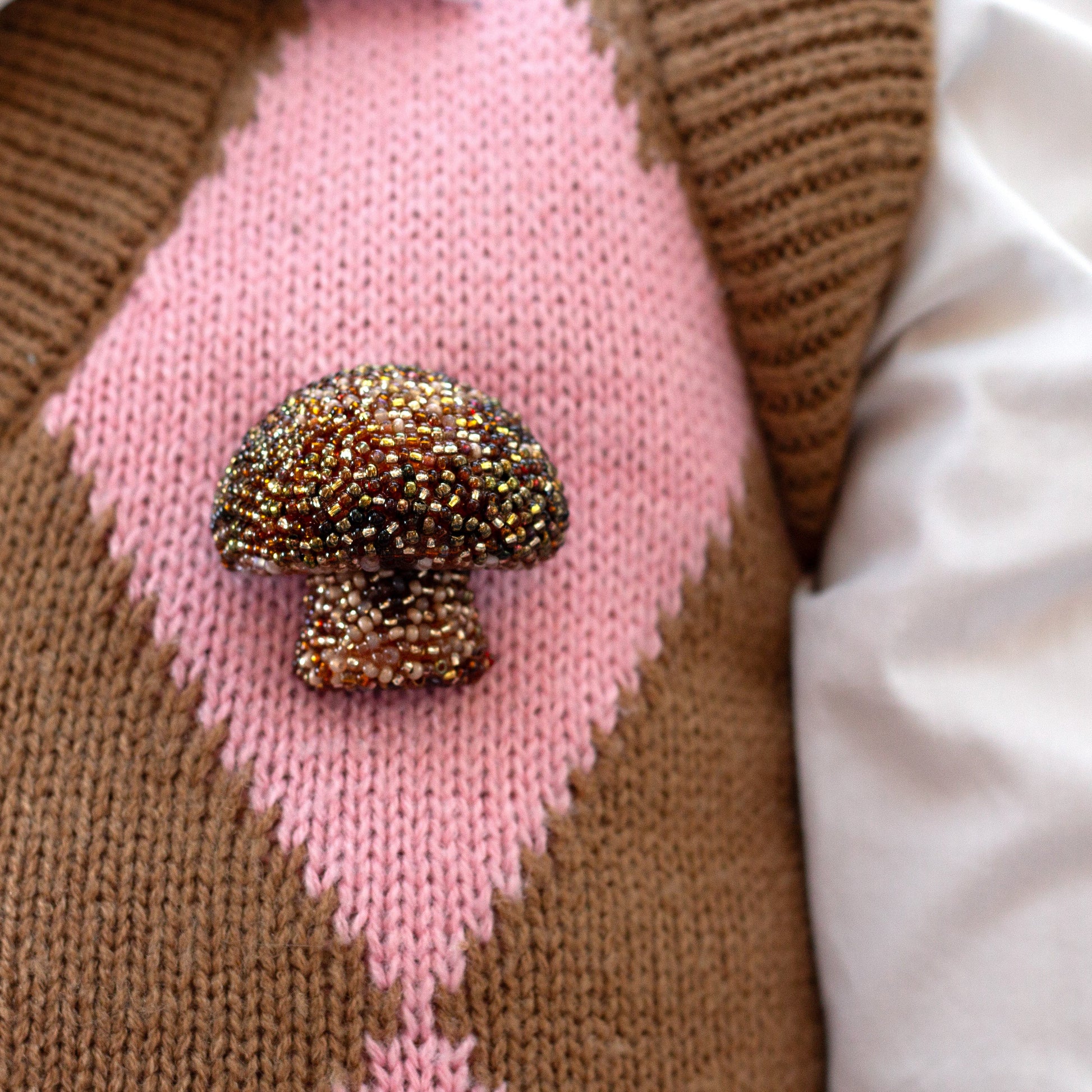 Closeup of a handmade beaded brown mushroom brooch worn on a diamond patterned vest.