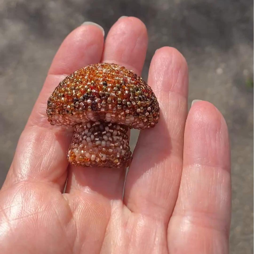 Hand holding a beaded brown mushroom brooch shown in the sunlight.