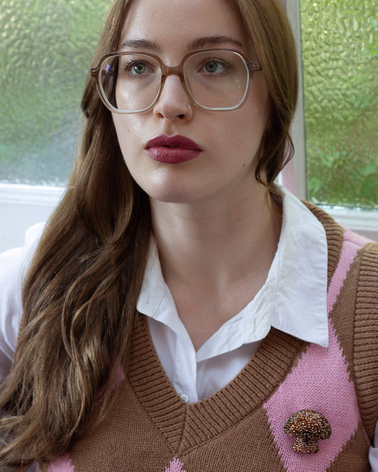 Handmade beaded brown mushroom brooch worn on a diamond patterned vest by a young woman.