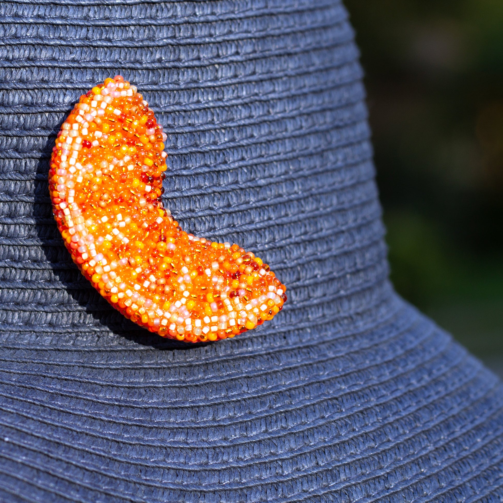 Closeup of a handmade beaded orange slice brooch worn on a blue summer hat.