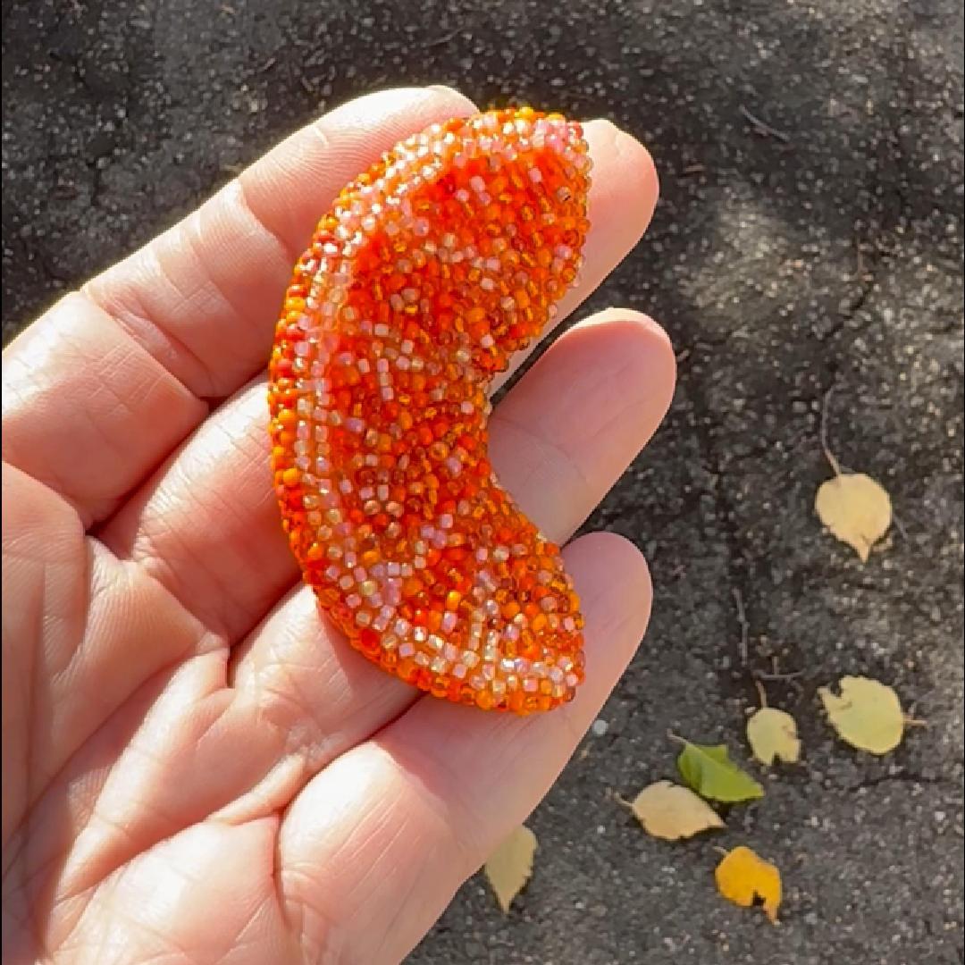 Hand holding a beaded orange slice brooch in the sunlight.