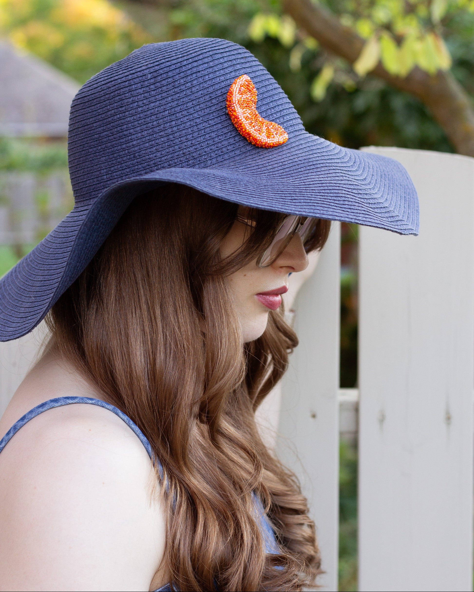 Handmade beaded orange slice brooch worn on a blue summer hat by a young woman.