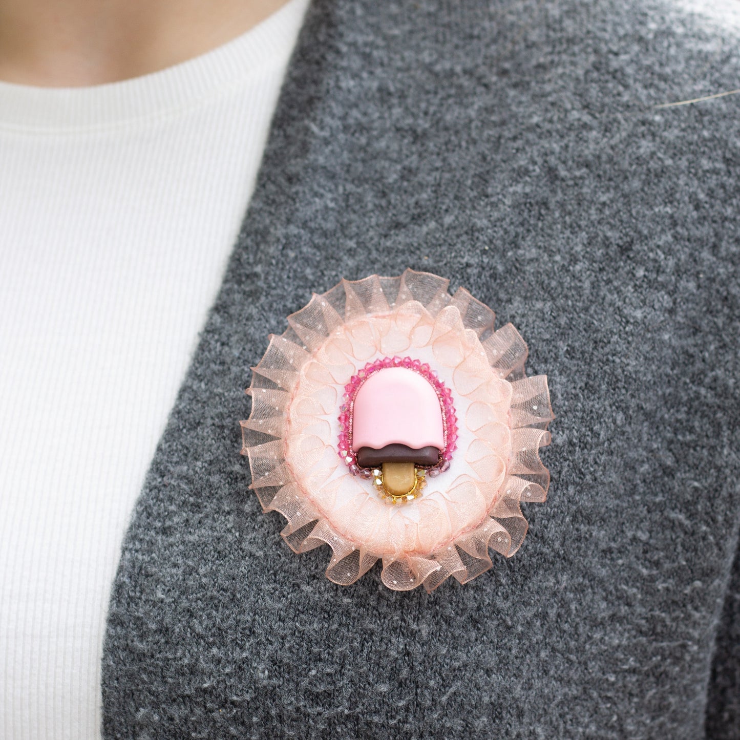 Closeup of a handmade brooch featuring a popsicle and crystal beads worn on a grey sweater.