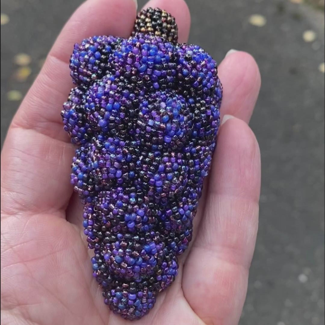 Video of a hand holding a purple beaded grape bunch brooch taken outside to show off the sparkle.