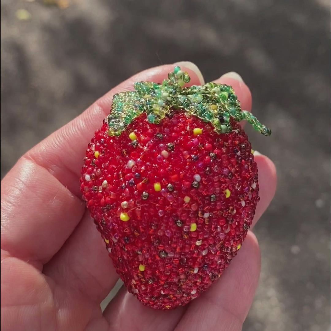 Video of a hand holding a beaded strawberry brooch taken outside to show off the sparkle.