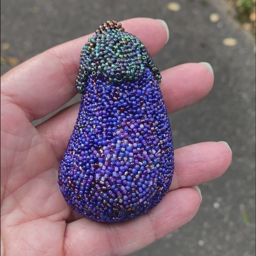 Video of a hand holding a beaded purple eggplant brooch taken outside to show off the sparkle.