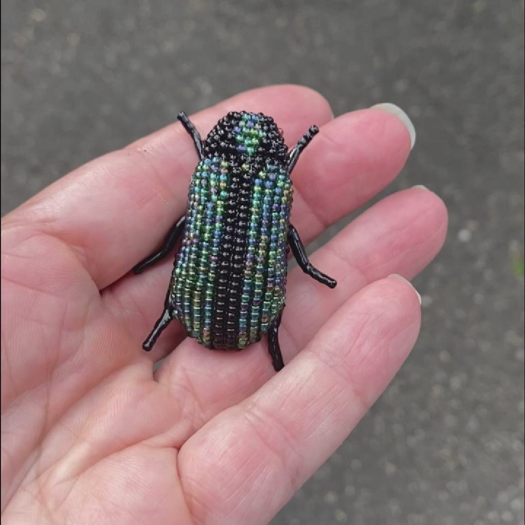 Video of a hand holding a green and black beaded beetle brooch taken outside to show off the sparkle.