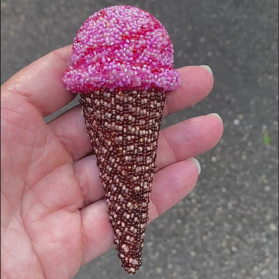 Video of a hand holding a pink beaded ice cream cone brooch taken outside to show off the sparkle.