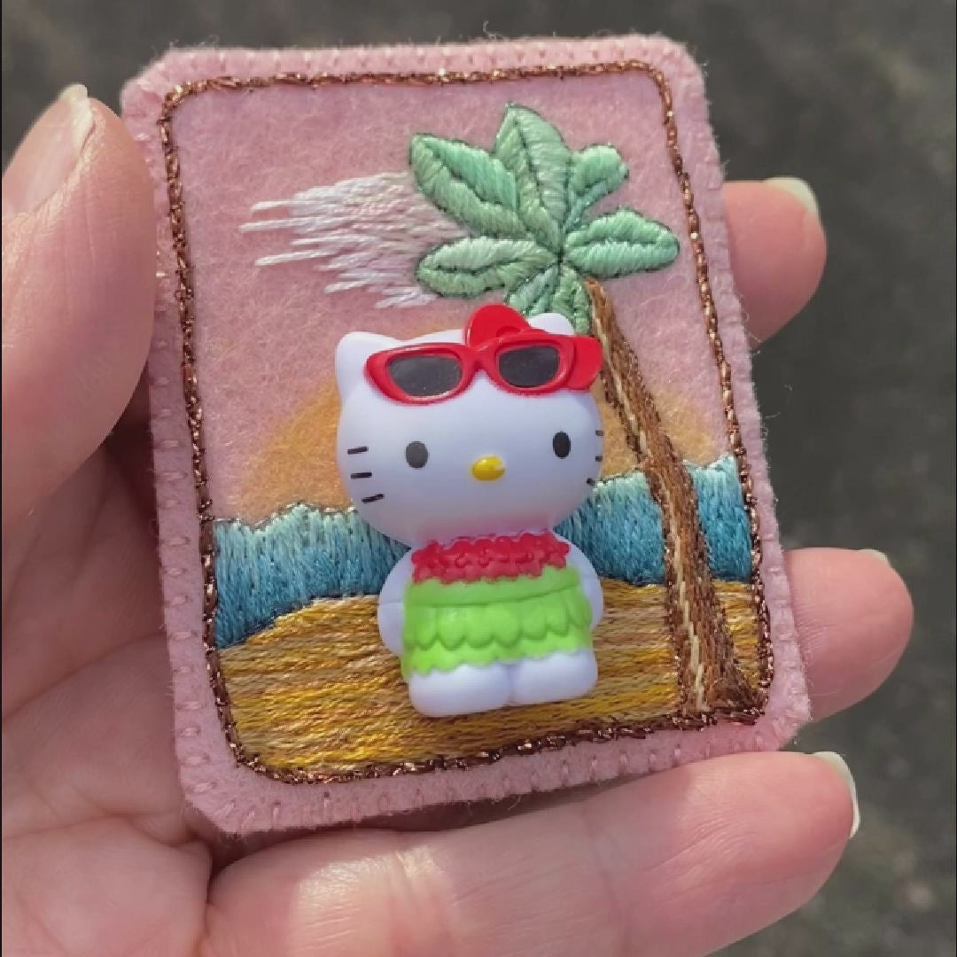 Video of a hand holding an embroidered Hello Kitty brooch taken outside to show off the sparkle.