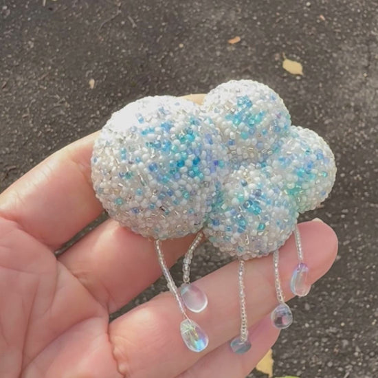 Video showing a beaded cloud brooch held in a hand, shot outside to show off the sparkle.