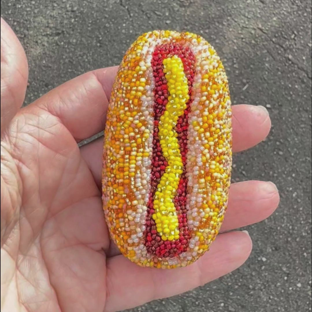 Video showing a handmade beaded hot dog brooch held in a hand outdoors to show off the sparkle.