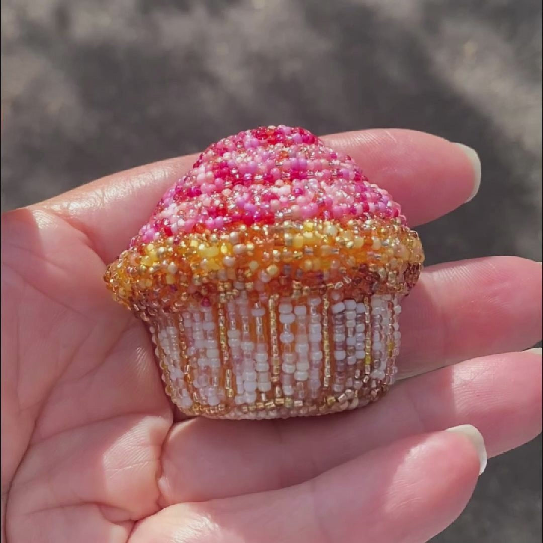 Video of a hand holding a beaded pink frosted cupcake brooch taken outside to show off the sparkle.