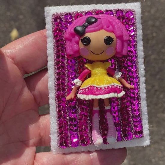Video of a hand holding a Lalaloopsy doll brooch covered in pink sequins taken outside to show off the sparkle.