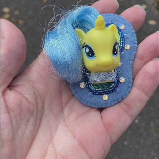 Video of a hand holding a beaded brooch featuring Lemony Gem My Little Pony taken outside to show off the sparkle.