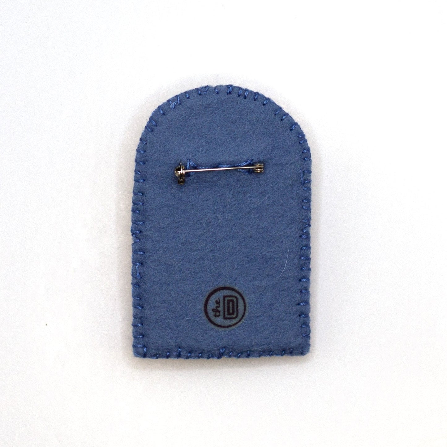 Back view of a handmade embroidered rainbow brooch featuring Pandy Paws on a white background showing pin fastener.